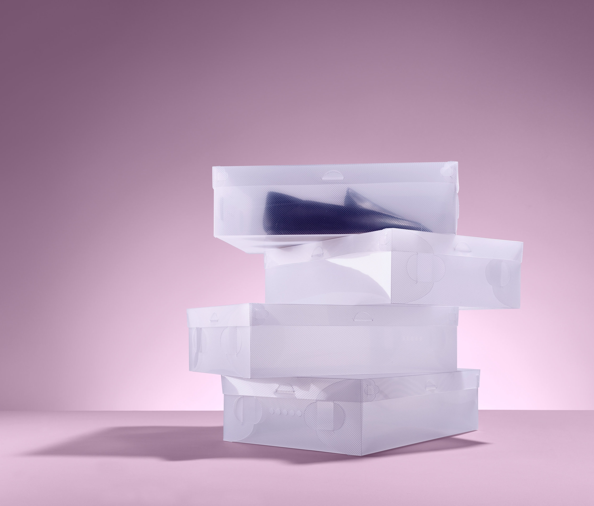 Čtyři úložné boxy na boty naskládané na sobě na růžovém pozadí.