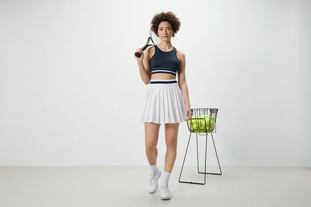 Žena drží tenisovou raketu a má na sobě modrou sportovní podprsenku »Crop Top«.