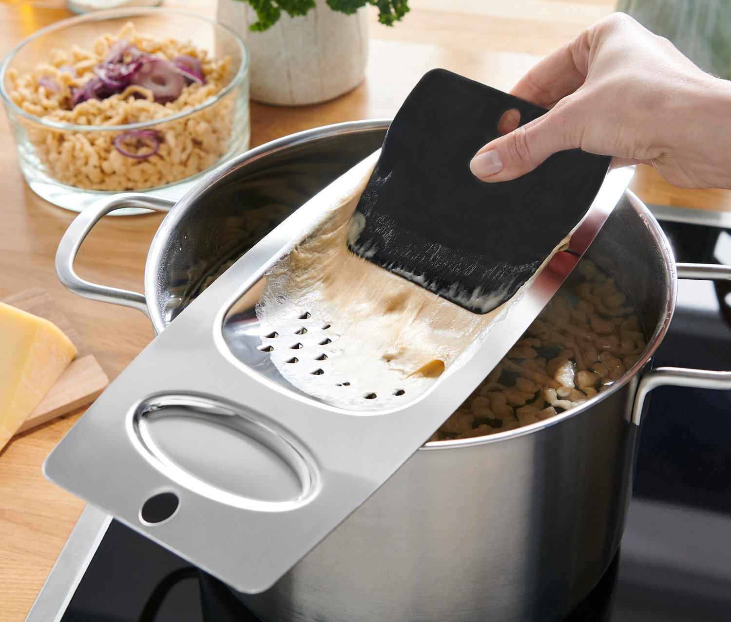 Ruka drží struhadlo na špecle nad hrncem s vařícími se špeclemi.