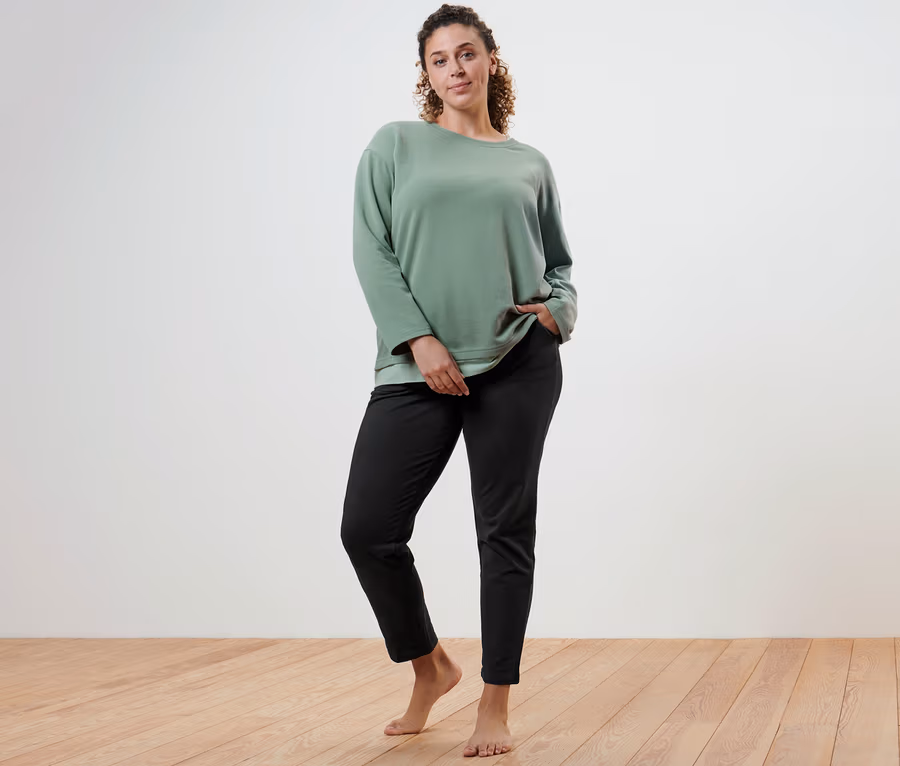 Žena pózuje v oversized fitness tričku s dlouhým rukávem a černých teplákových kalhotách.