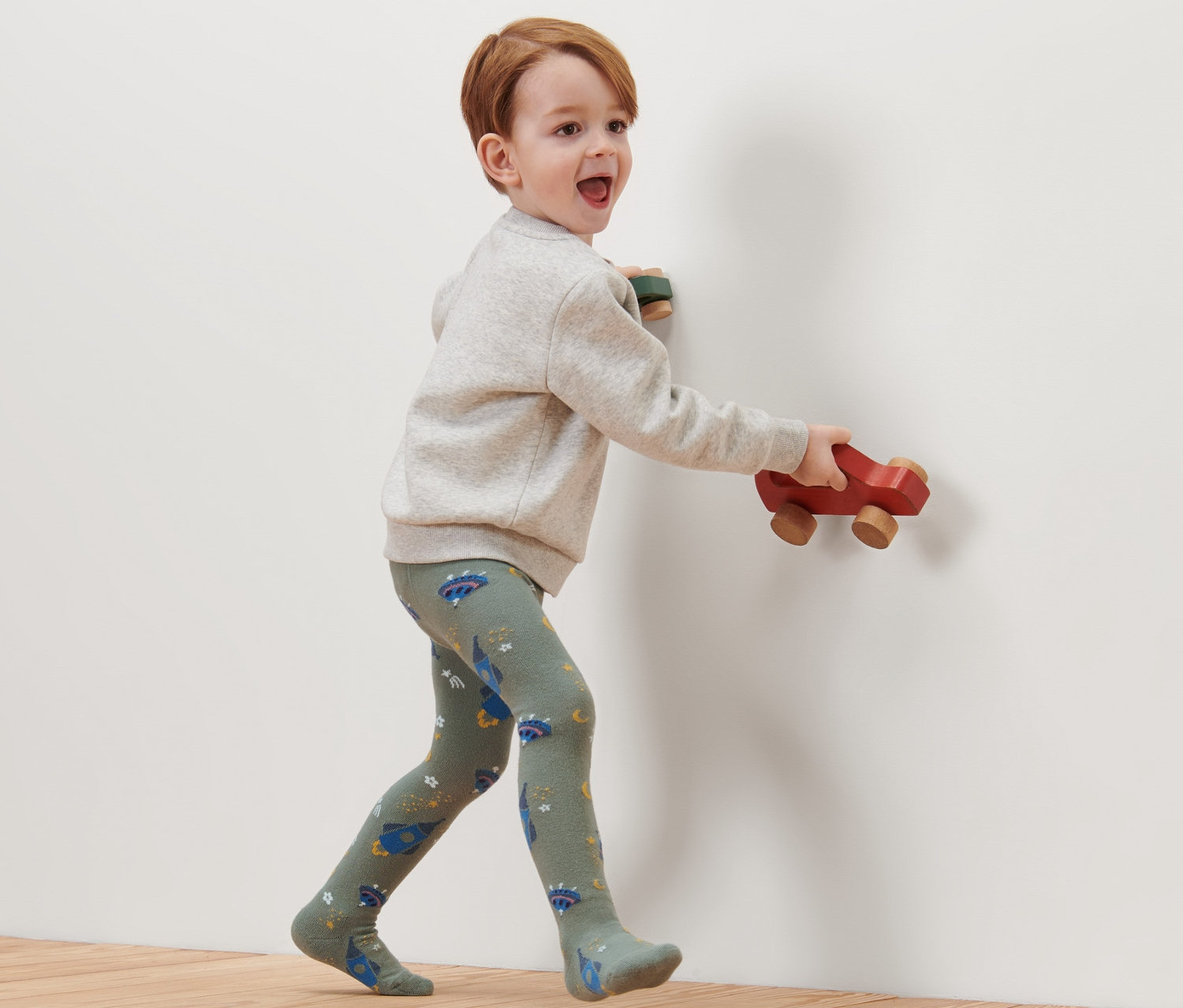 Chlapec kráčí po dřevěné podlaze a má na sobě bavlněné punčocháče s motivem vesmíru.