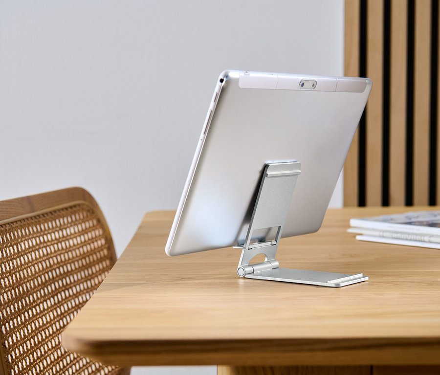 Tablet je opřený o stojan na smartphone a tablet na dřevěném stole.