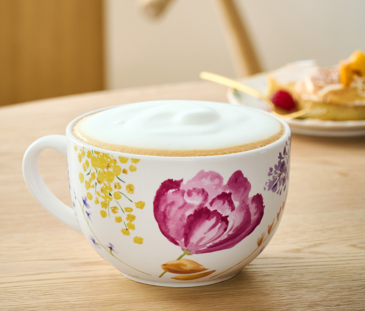 Květinový šálek na kávu s mlékem na stole.