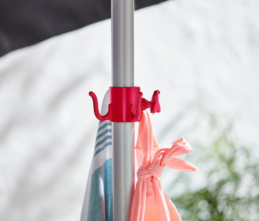 Na tyči je červený držák, na kterém visí ručník s modrými pruhy a růžové oblečení.