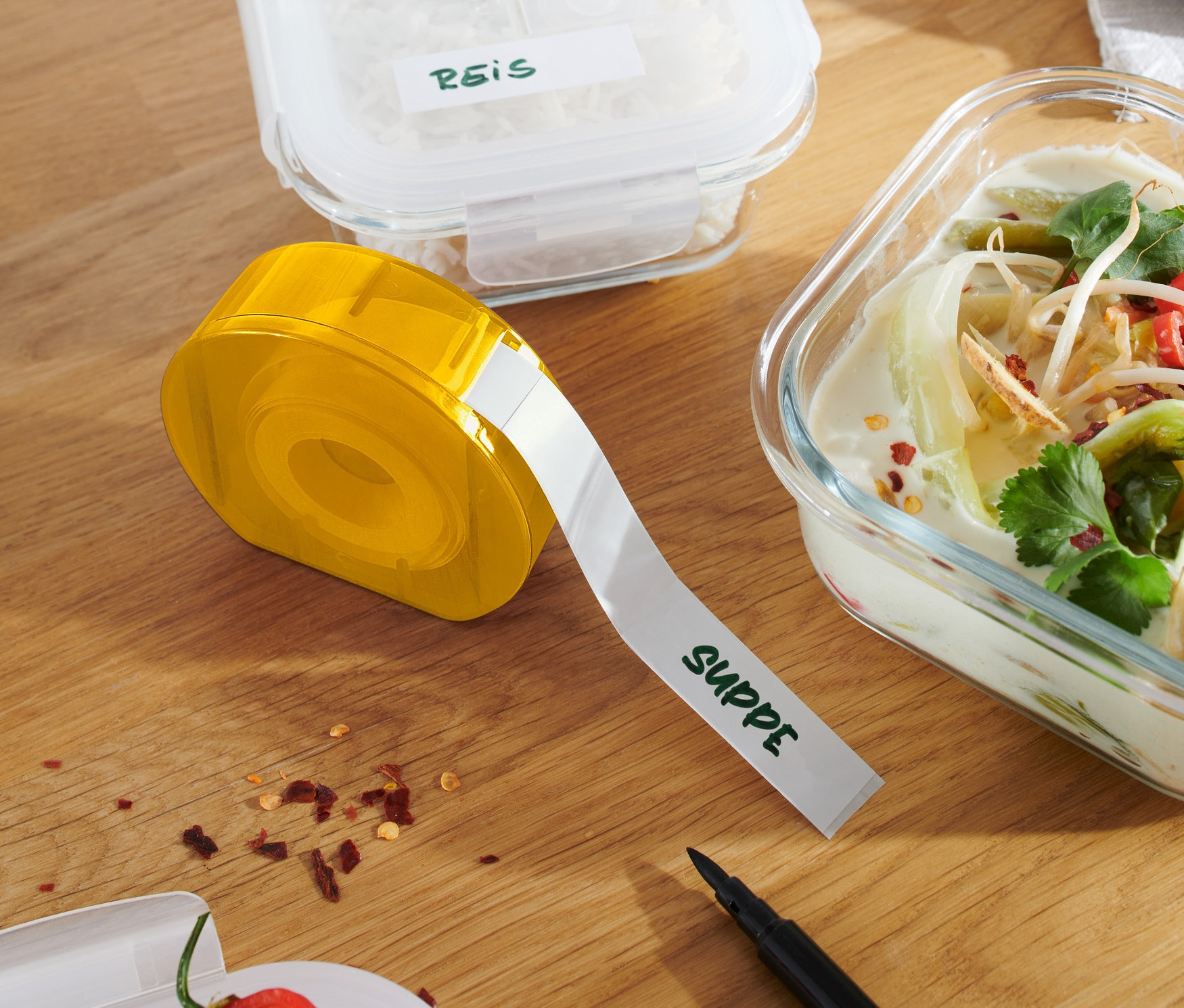 Žlutý zásobník na etikety na dřevěném stole vedle nádob s rýží a polévkou.