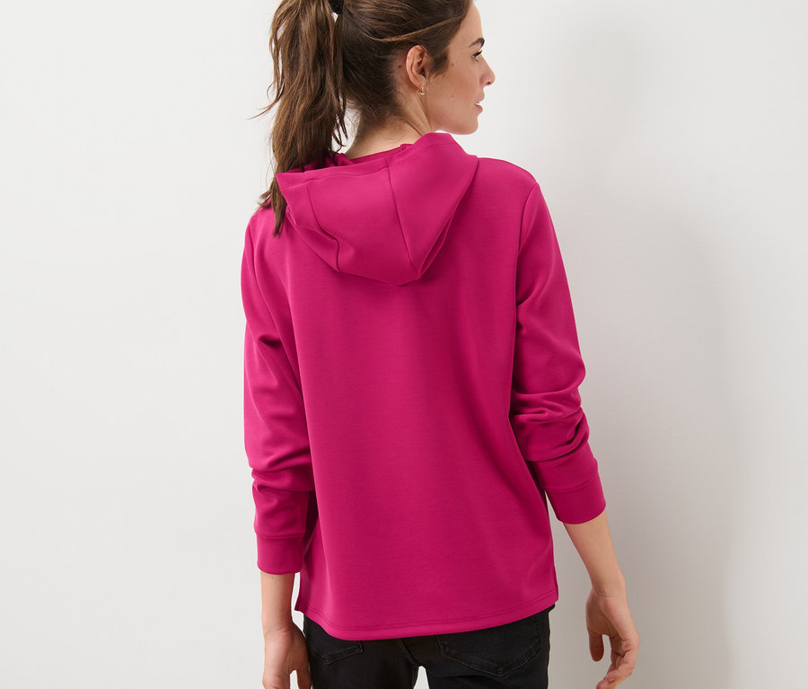 Žena zády k fotoaparátu má na sobě růžovou mikinu s kapucí z modalové směsi.