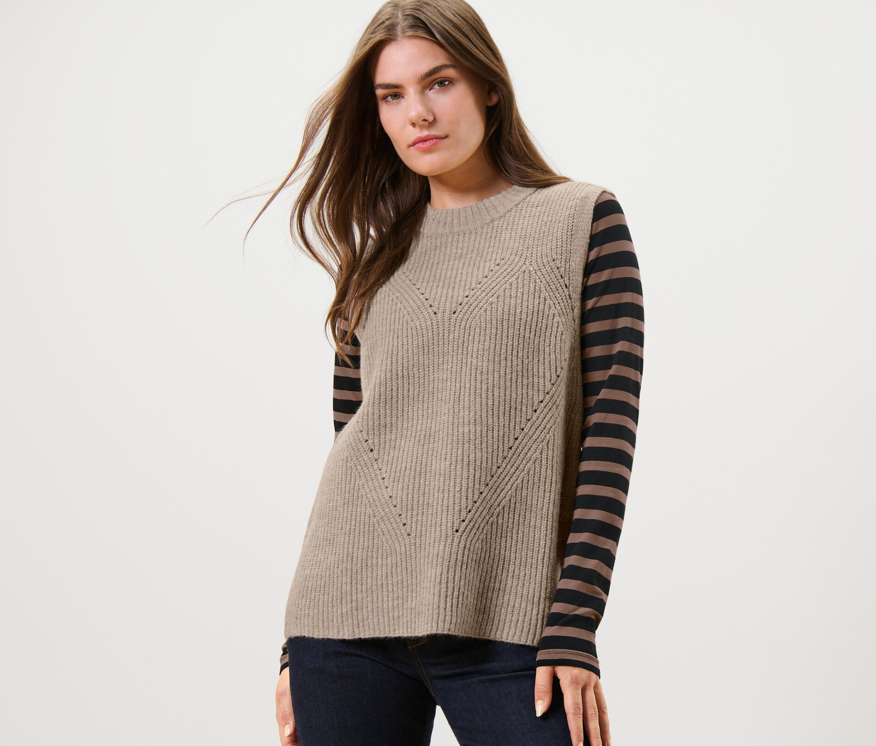 Žena má na sobě pletenou vestu béžové barvy s melírem.