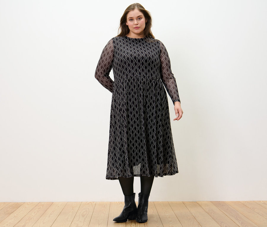 Žena stojí a má na sobě síťované šaty s potiskem.