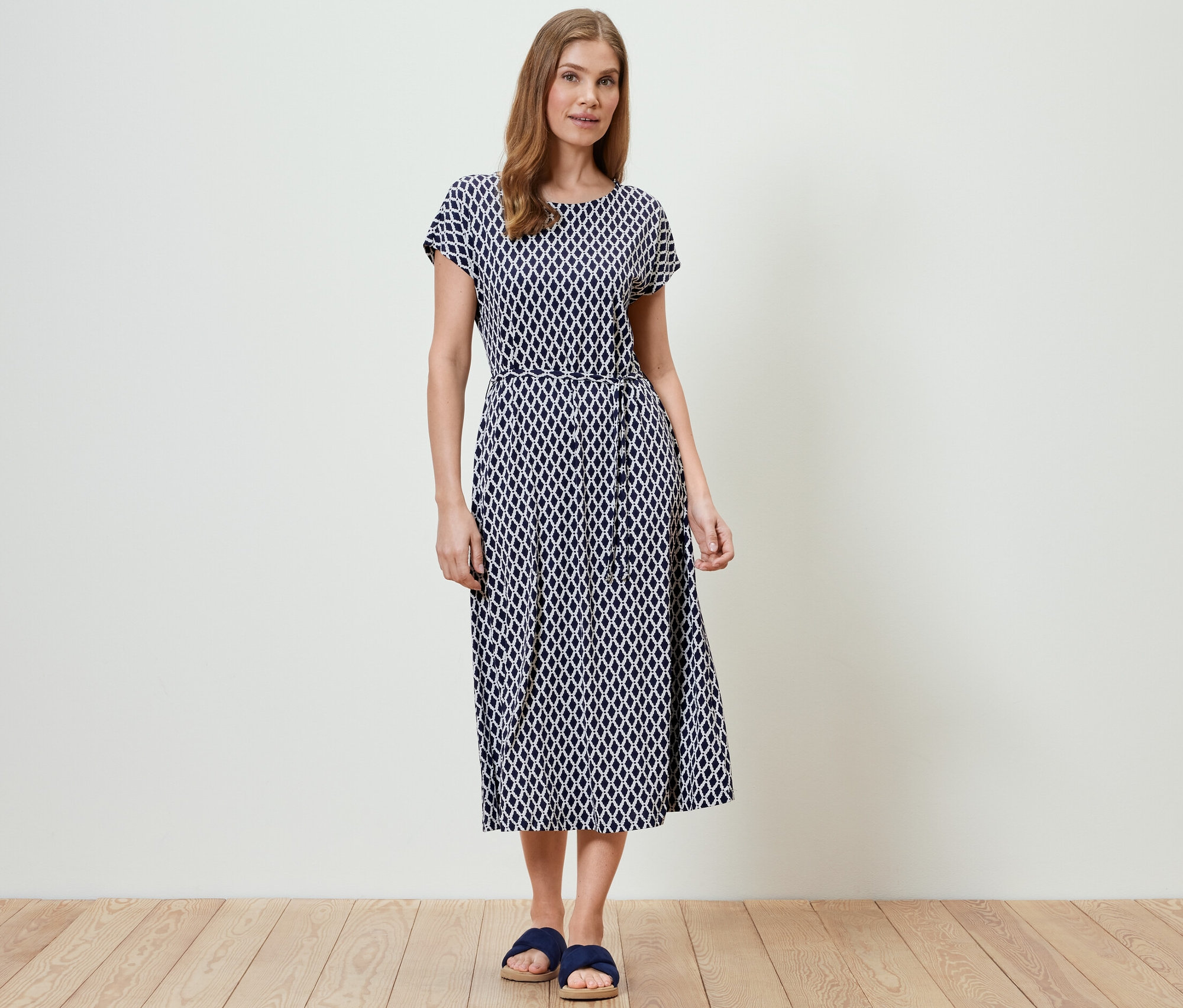 Žena stojí a má na sobě žerzejové šaty s potiskem.