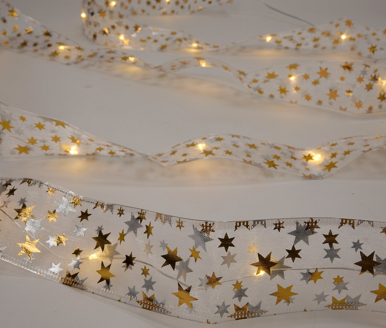 Tři stuhy s LED světýlky a hvězdami na bílém pozadí.