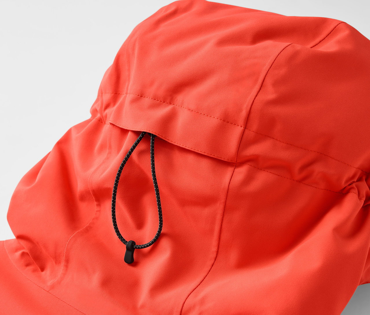 Detail kapuce oranžové bundy se stahovací šňůrkou.