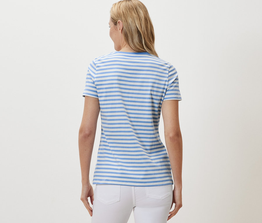 Zezadu je vidět žena s blond vlasy v tričku s proužky ve světle modré a bílé barvě.