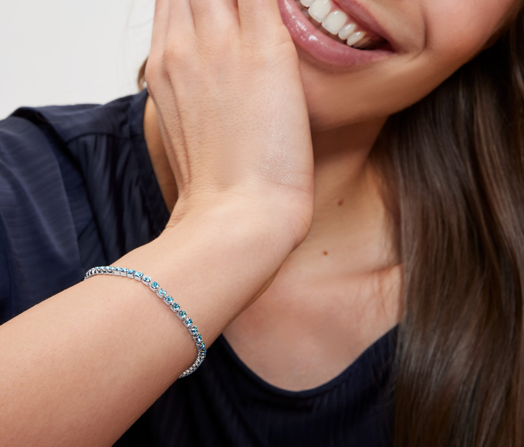 Žena se usmívá a dotýká se tváře, na zápěstí má náramek s článkovým řetízkem.