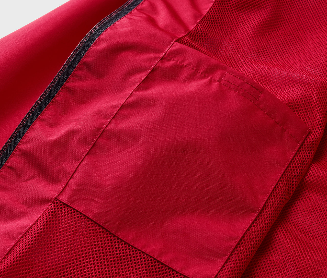 Detail červené bundy do deště s kapsou.