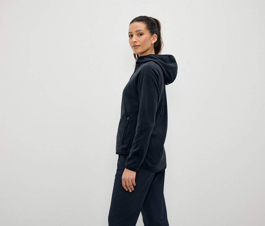 Žena v tmavě modré fleecové mikině s kapucí a kalhotách, stojící bokem.