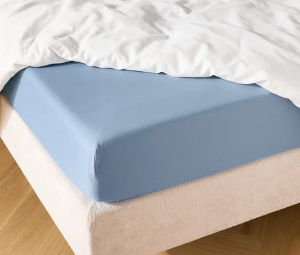 Světle modré napínací prostěradlo na posteli s bílou přikrývkou.