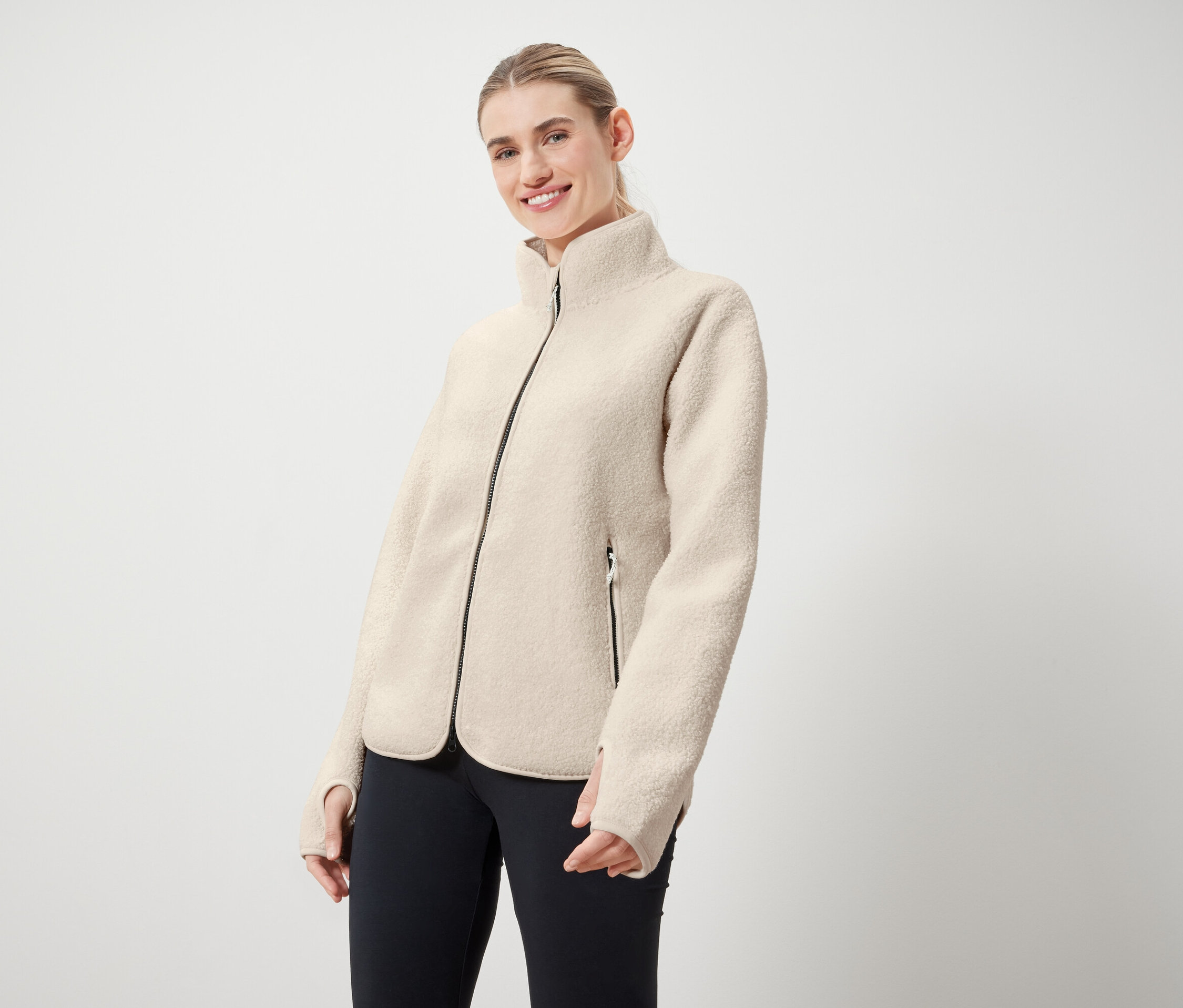 Žena má na sobě krémovou bundu s černým zipem a černé legíny.