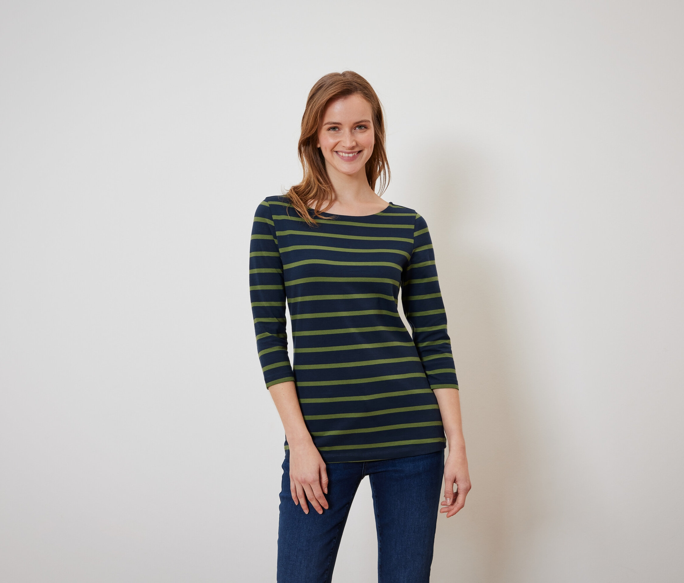 Žena s hnědými vlasy pózuje v modrozeleném pruhovaném tričku a modrých džínách.