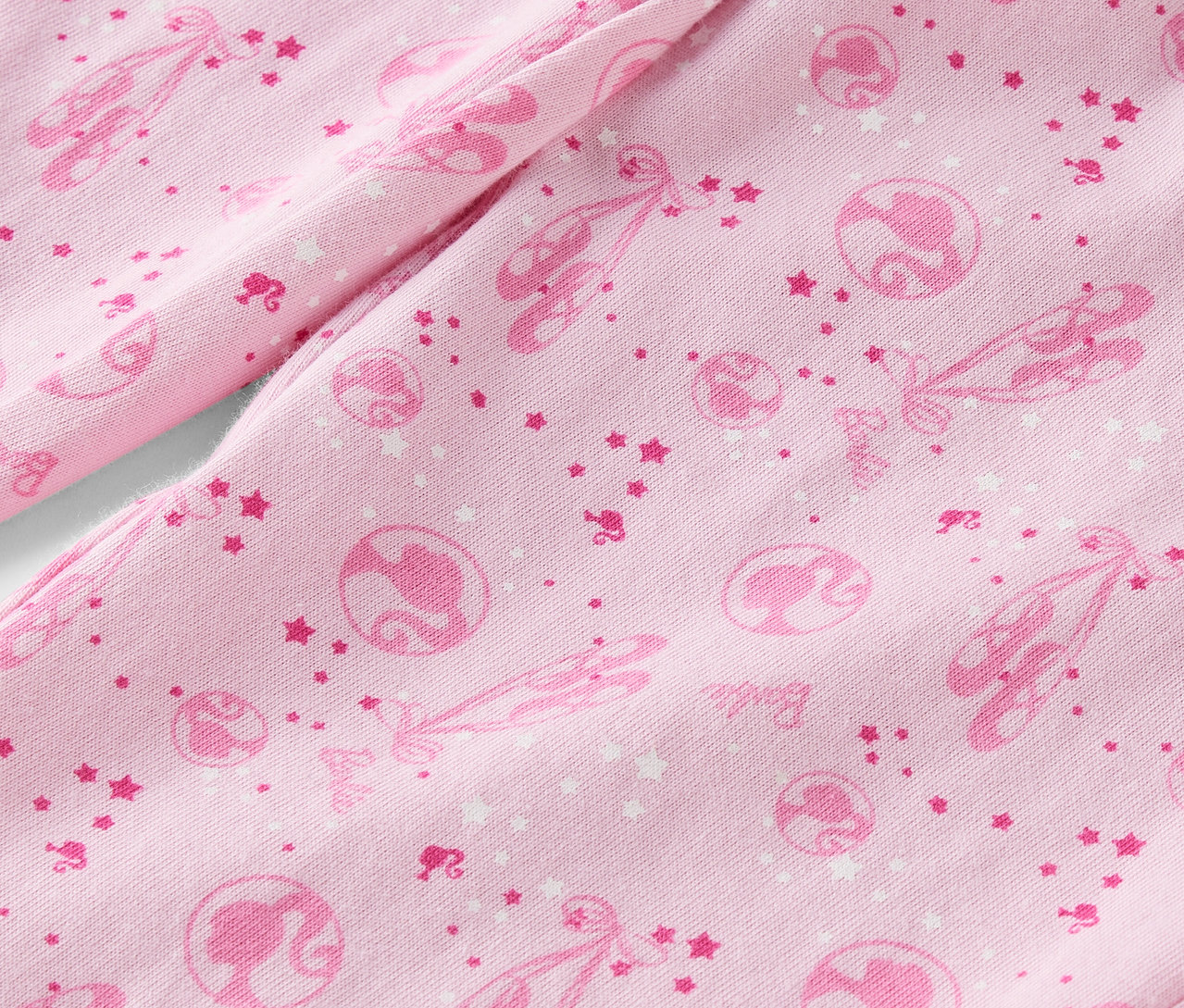 Detail růžové látky s potiskem baletek, hvězd a siluet Barbie.