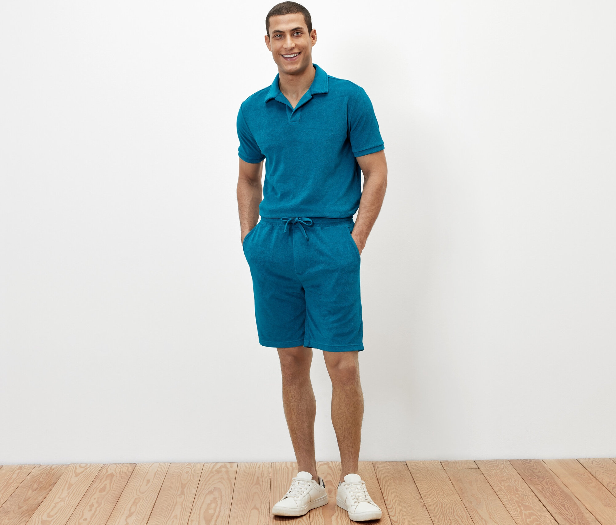 Muž stojí a má ruce v kapsách froté šortek petrolejové barvy.