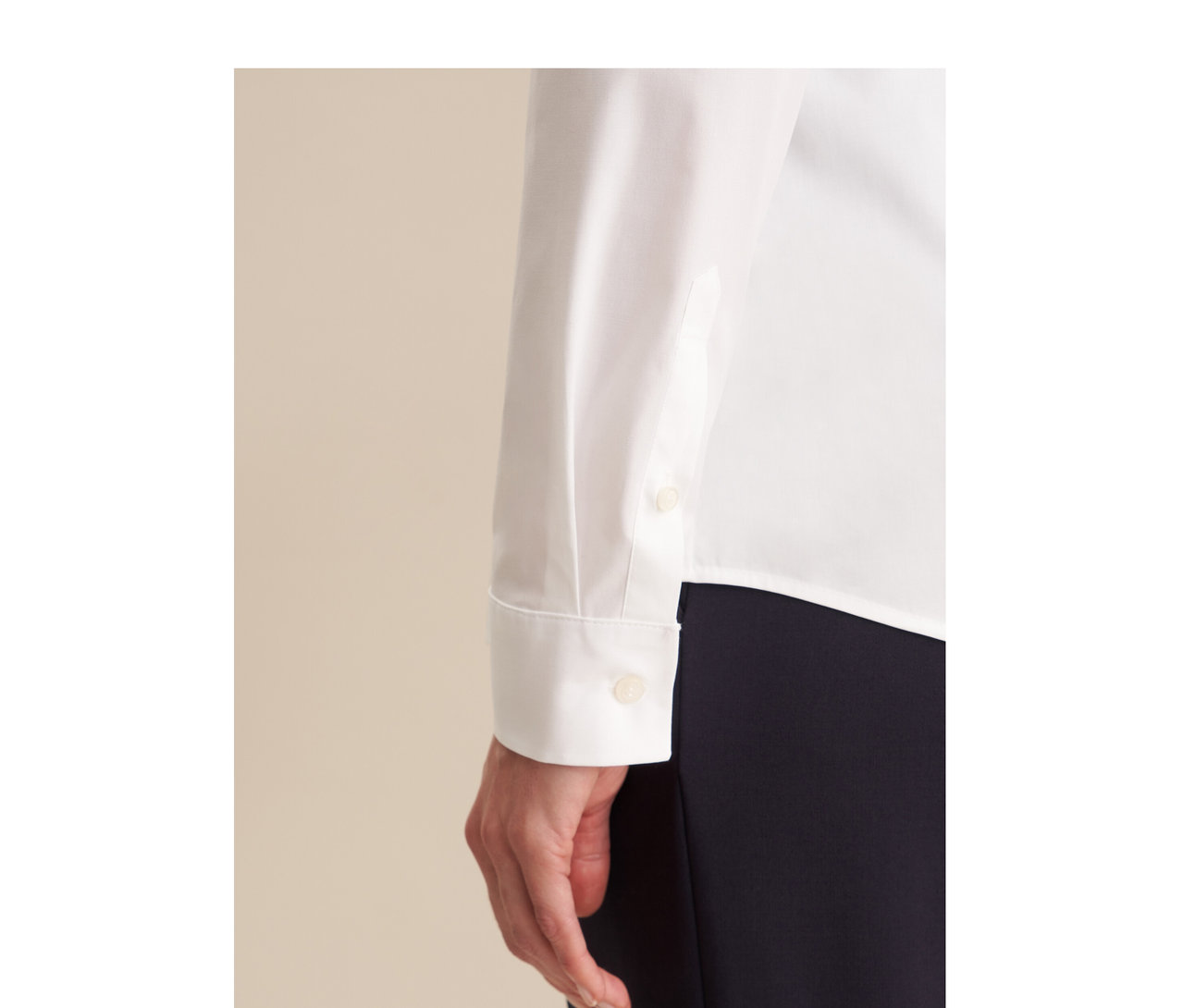Detail osoby v bílé halence slim fit Seidensticker s knoflíkovými manžetami a tmavých kalhotách. Je vidět ruka.