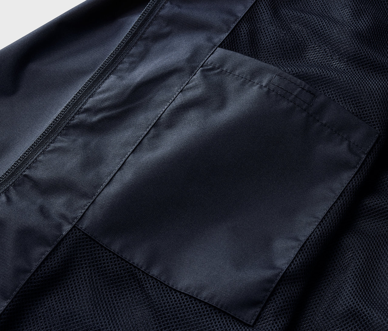 Detail námořnicky modré bundy do deště s kapsou.