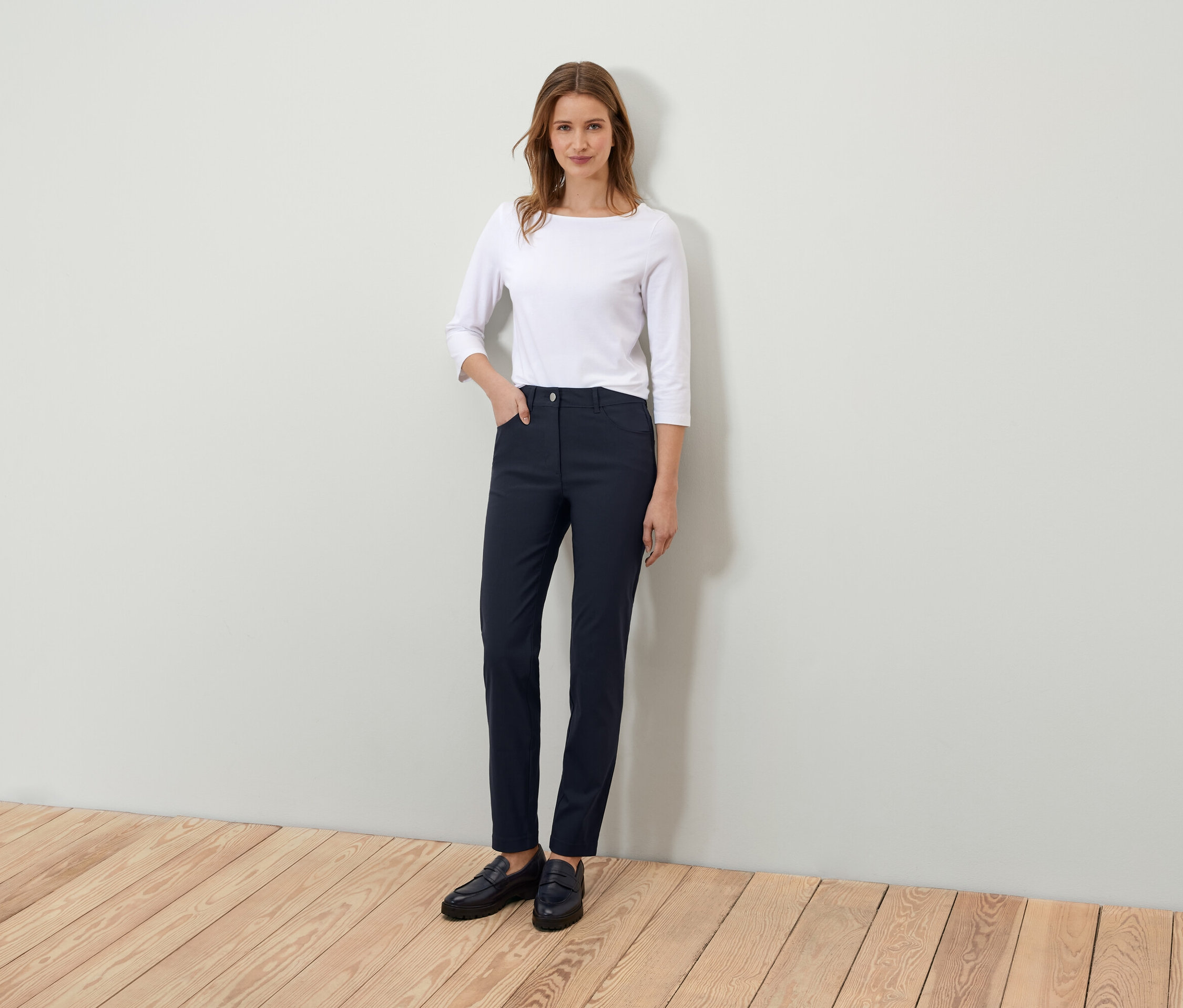Žena stojí a pózuje v bílém tričku s tříčtvrtečním rukávem a tmavě modrých kalhotách.