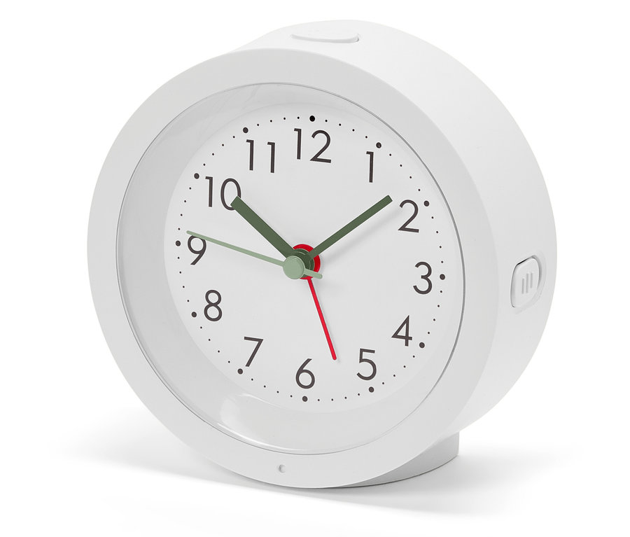 Bílý budík s analogovým ciferníkem a zelenými ručičkami ukazuje čas.