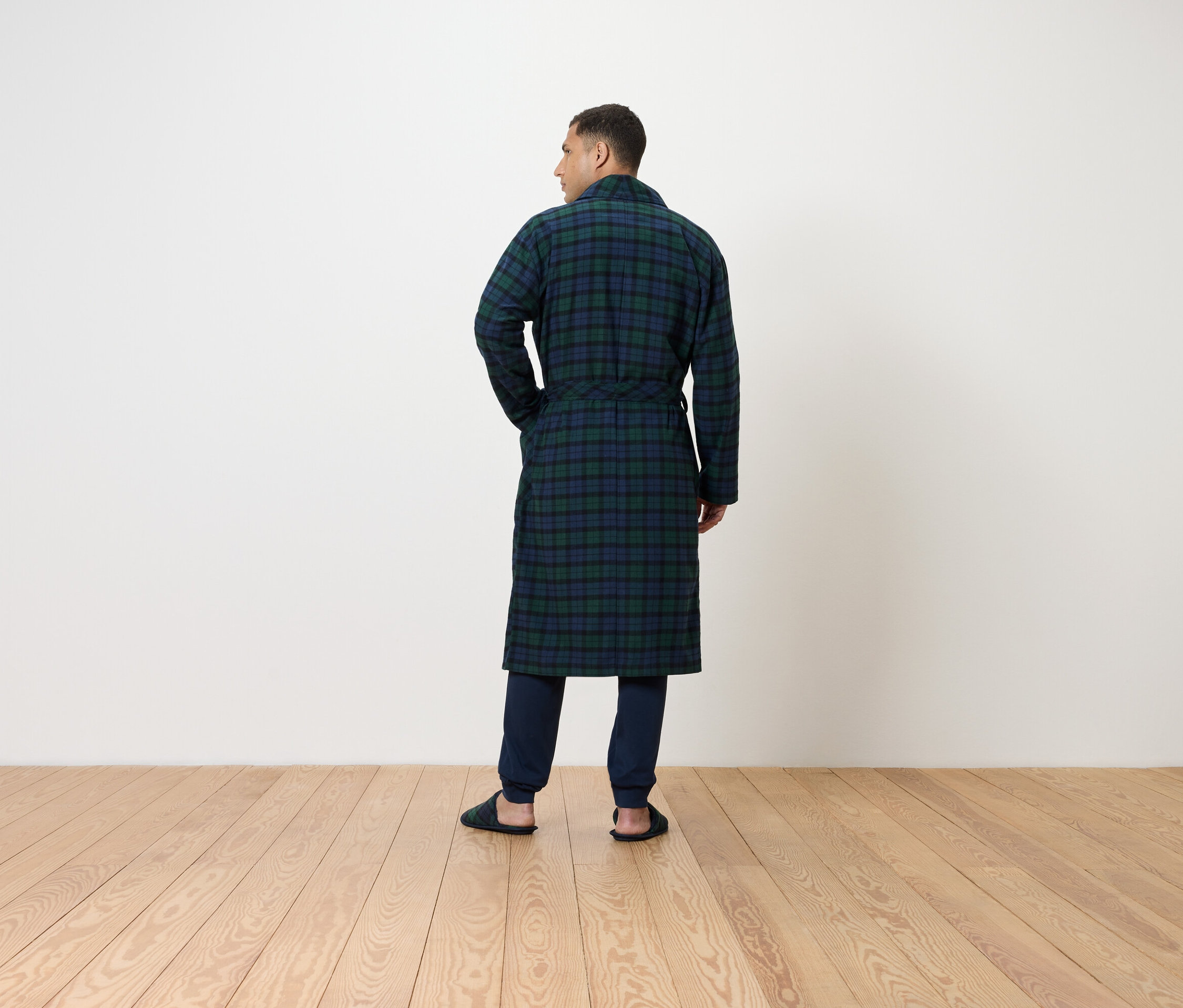 Muž zády k fotoaparátu má na sobě dlouhý, kostkovaný župan a tmavé kalhoty.