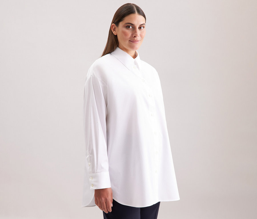 Žena má na sobě bílou dlouhou halenku oversize Seidensticker.