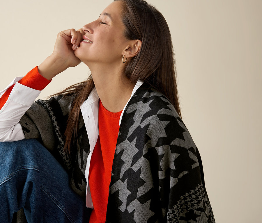 Žena sedí a má na sobě oranžový svetr z jemného úpletu merino.