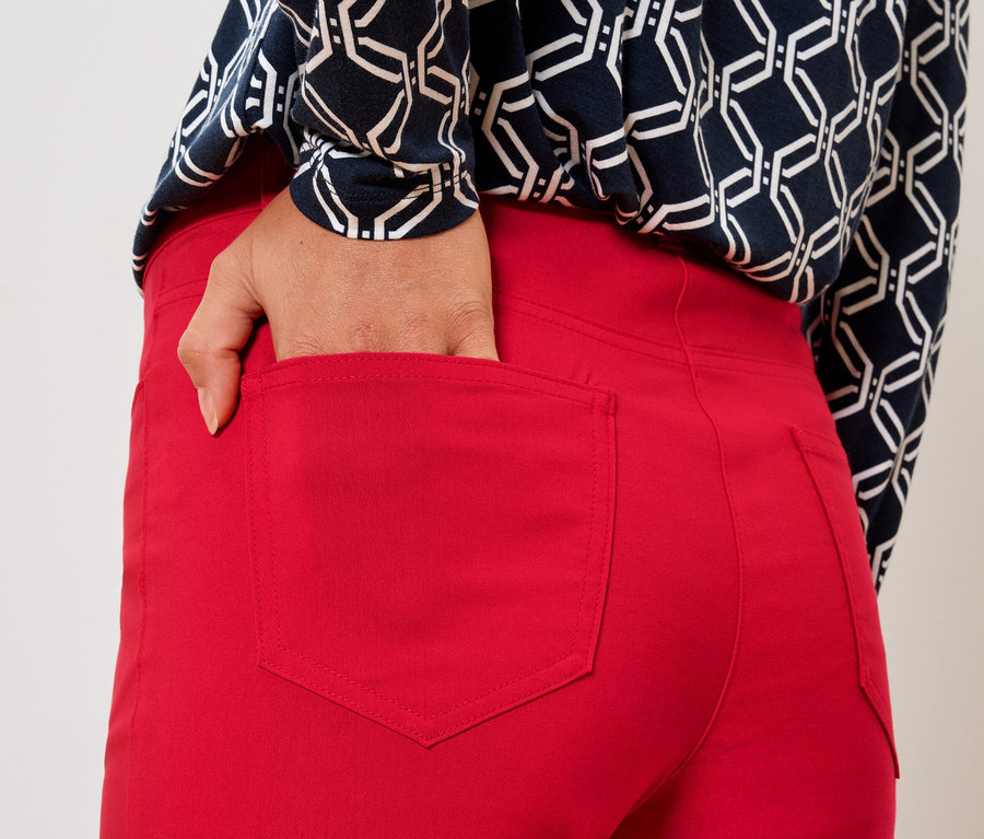 Žena strká ruku do zadní kapsy červených kalhot.