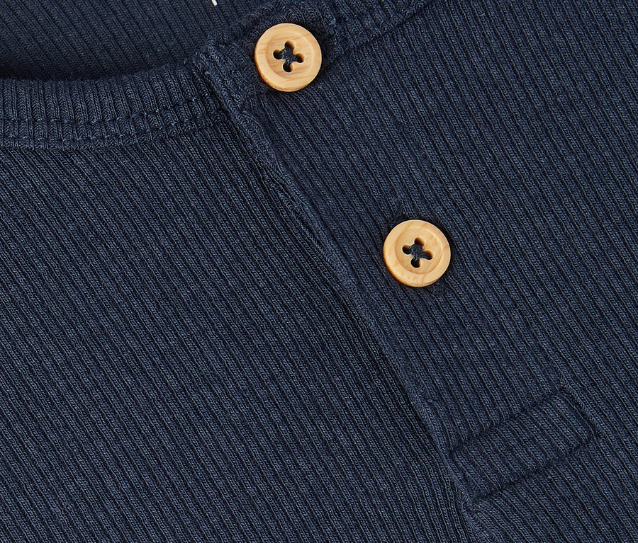 Detailní záběr na tmavě modrou žebrovanou košili se dvěma světle hnědými knoflíky a nápisem "name it" v levém horním rohu.