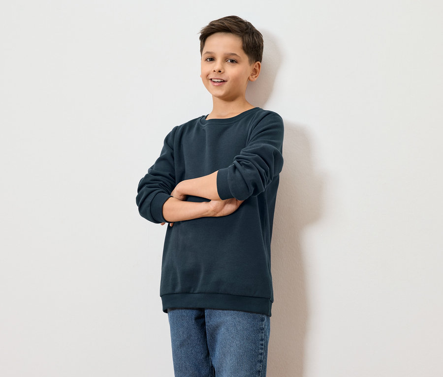 Chlapec stojí s rukama zkříženýma před bílou zdí.