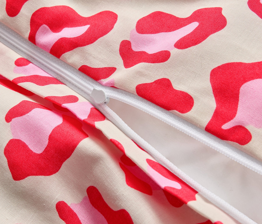 Detailní záběr částečně otevřeného zipu na látce s růžovými a červenými skvrnami.