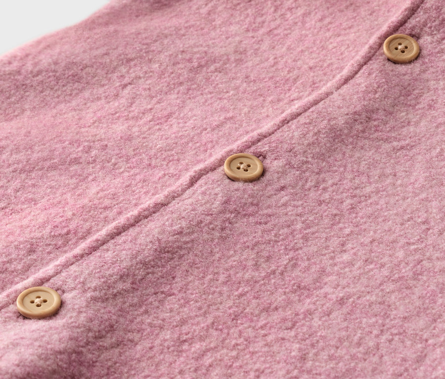 Detail růžové pleteniny se třemi světle hnědými knoflíky.