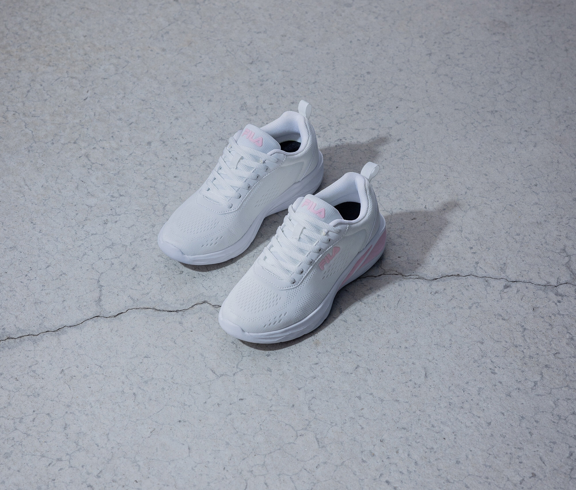 Dvě bílé tenisky Fila s růžovým logem leží na šedém pozadí.