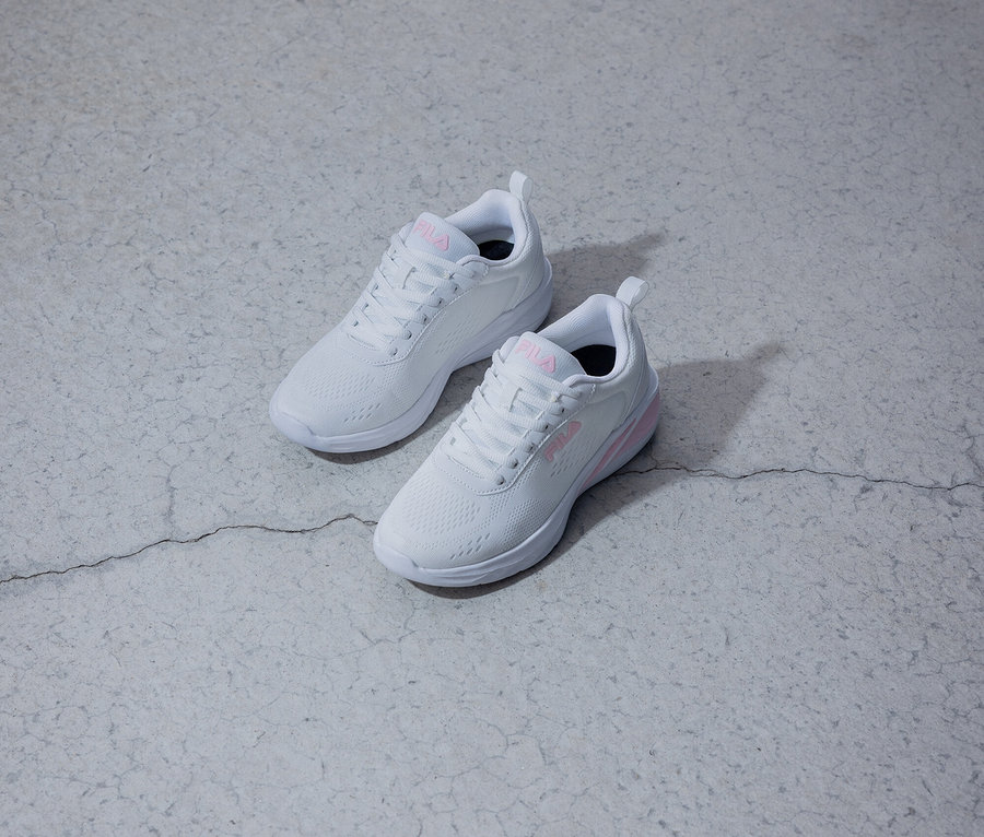 Dvě bílé tenisky Fila s růžovým logem leží na šedém pozadí.