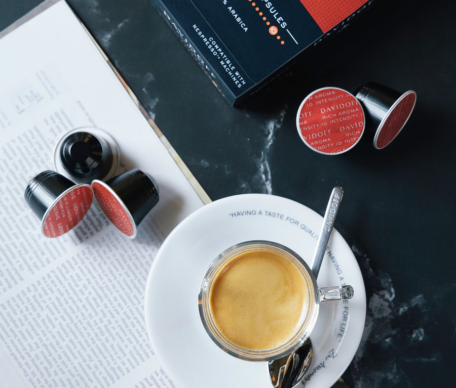 Espresso v šálku na podšálku s lžičkou vedle balení DAVIDOFF CAFÉ Rich Aroma a kávových kapslí.