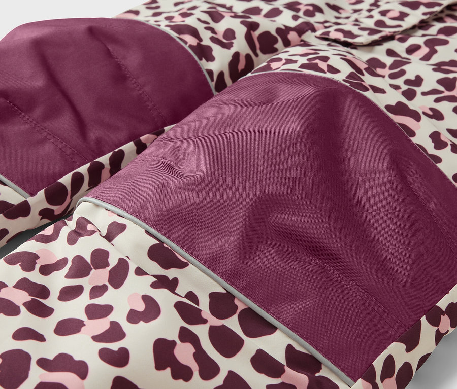 Detail oděvu s leopardím vzorem v béžové, tmavě fialové a růžové barvě. Má tmavě fialové nášivky na kolenou/loktech s reflexními proužky.
