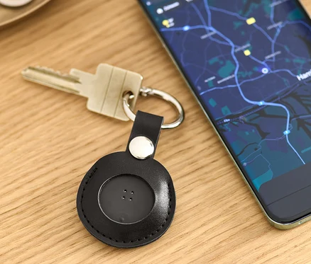 Na stole leží klíče s černým chytrým lokátorem s přívěskem a mobilní telefon s mapou.
