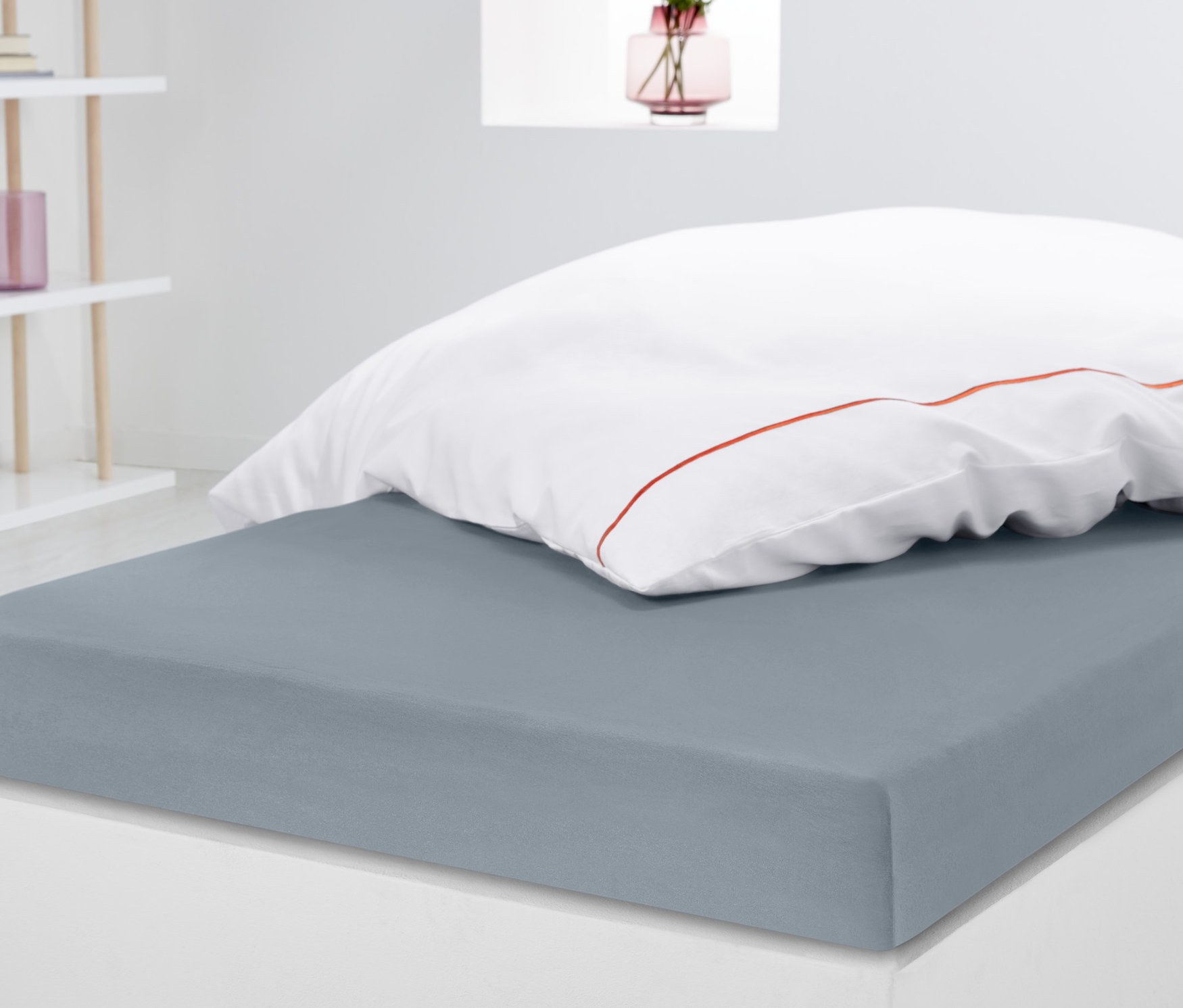 Šedé jerseyové napínací prostěradlo standardní velikosti na matraci s bílým polštářem.