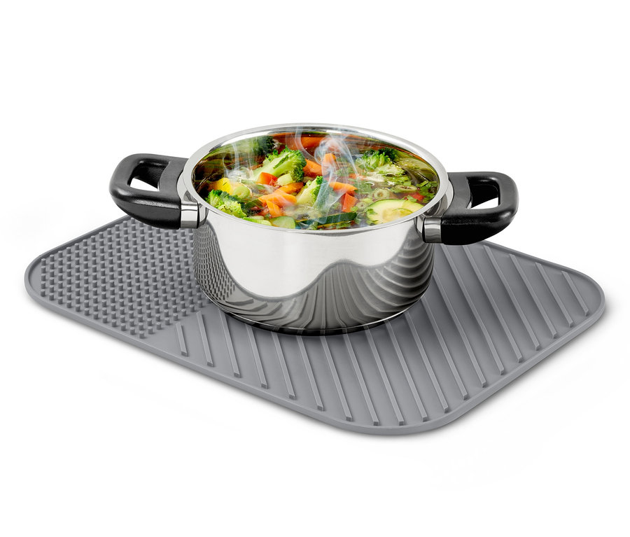 Nerezový hrnec plný zeleninové polévky stojí na silikonové odkapávací podložce na nádobí.