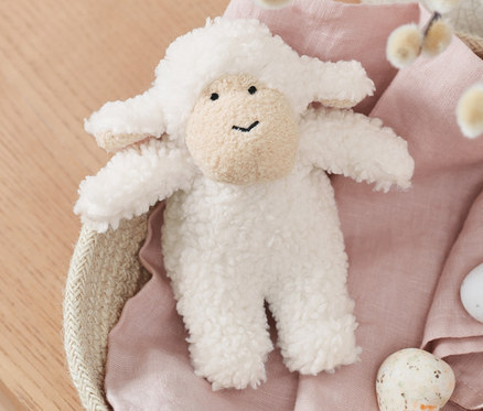 Plyšová ovečka vydávající zvuky leží v košíku s vrbovými větvičkami a malovanými vajíčky.