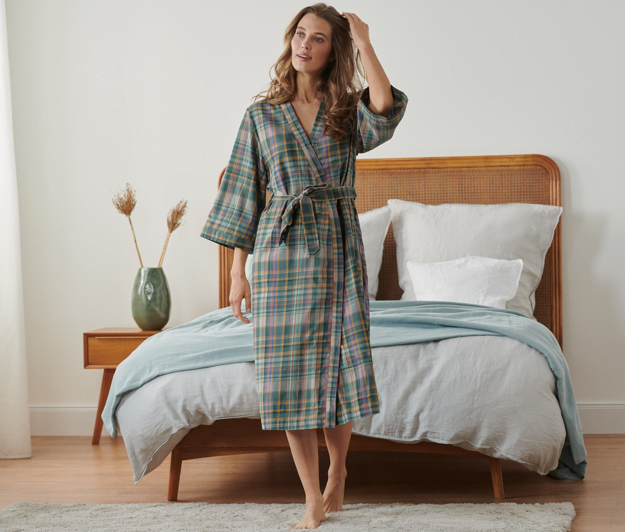 Žena má na sobě župan a stojí v ložnici.