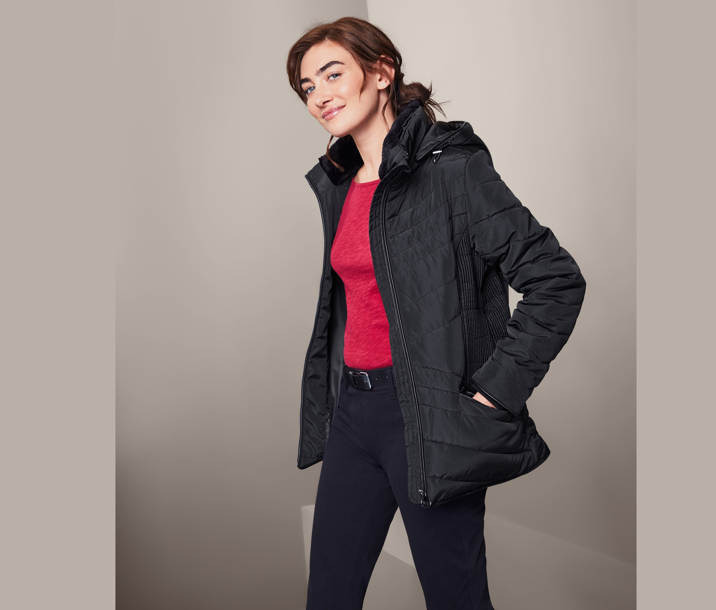 Žena pózuje v černé prošívané bundě.