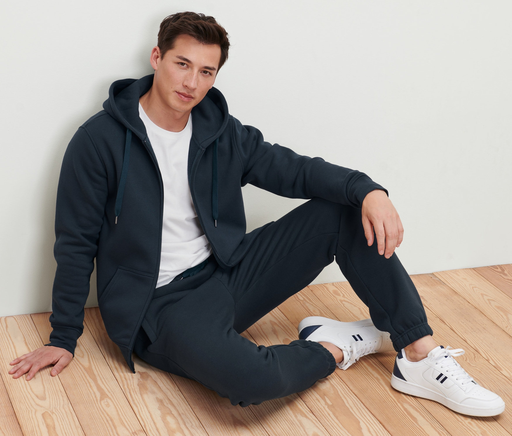 Muž sedí na podlaze a má na sobě bundu s kapucí.