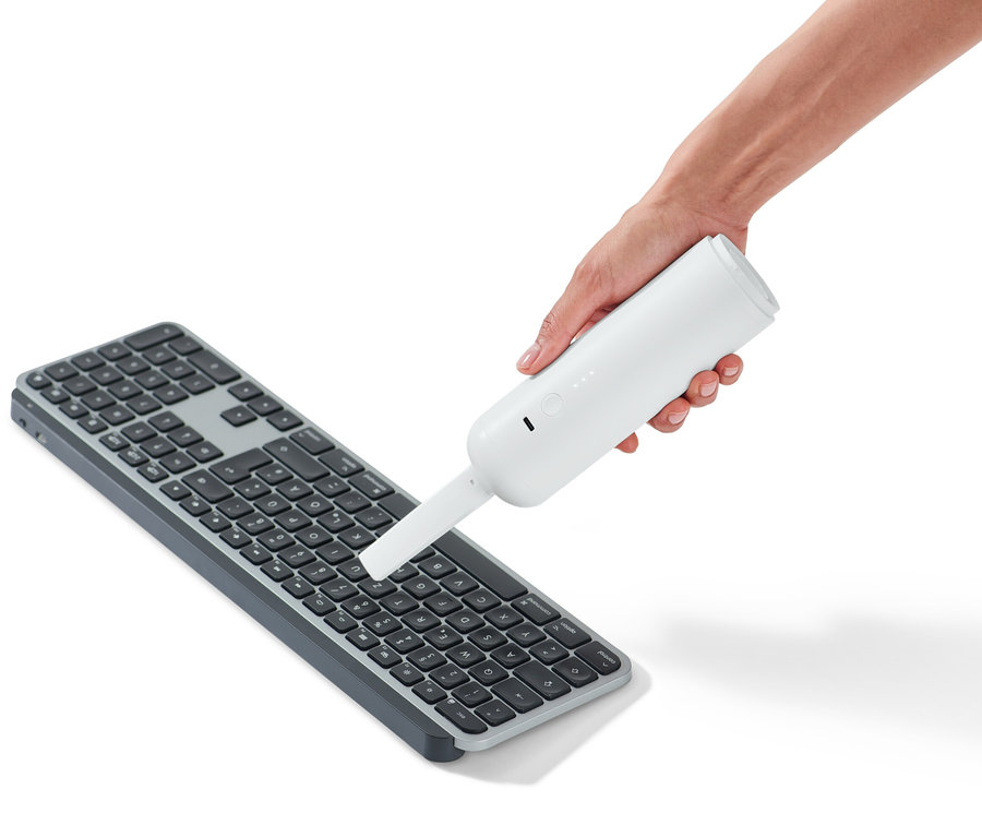 Ruka drží akumulátorový ruční vysavač nad klávesnicí.