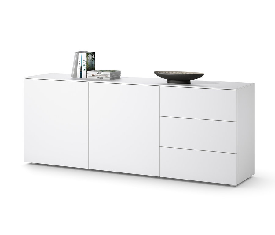 Bílá komoda se třemi zásuvkami a dvířky, na které leží knihy a miska.