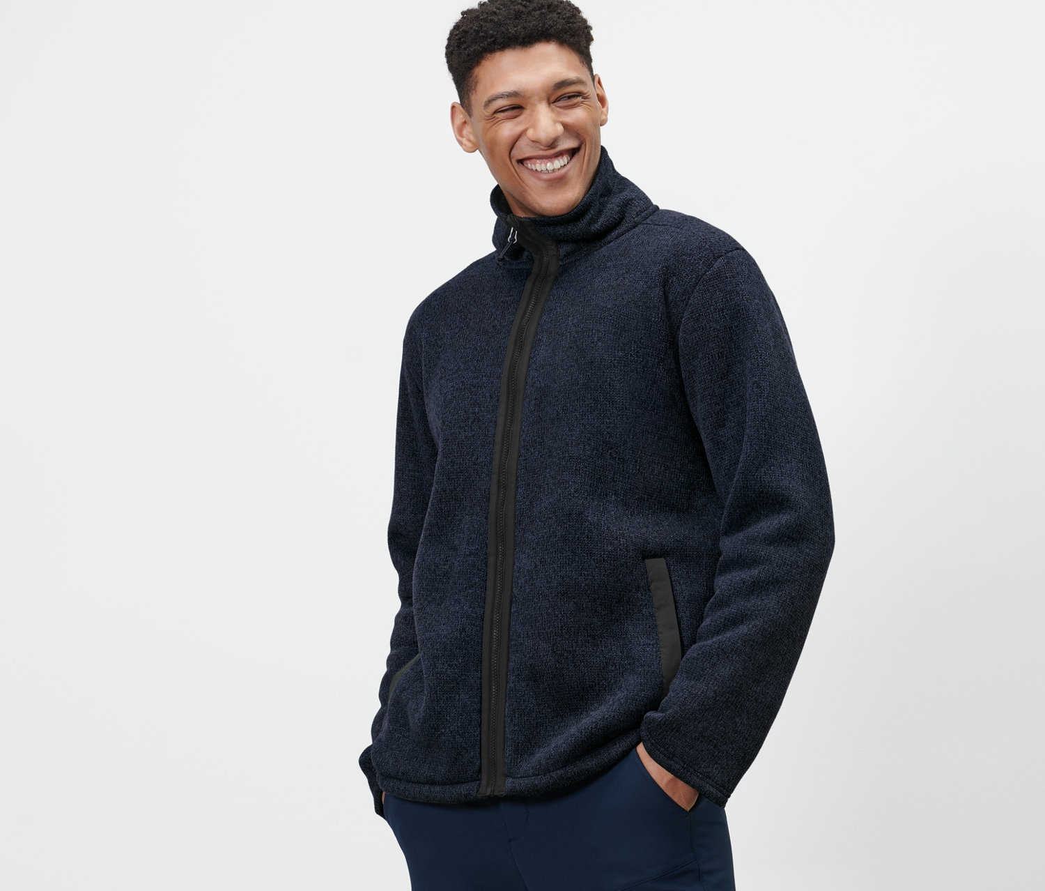 Muž s rukama v kapsách pózuje v bundě z pleteného fleecu.